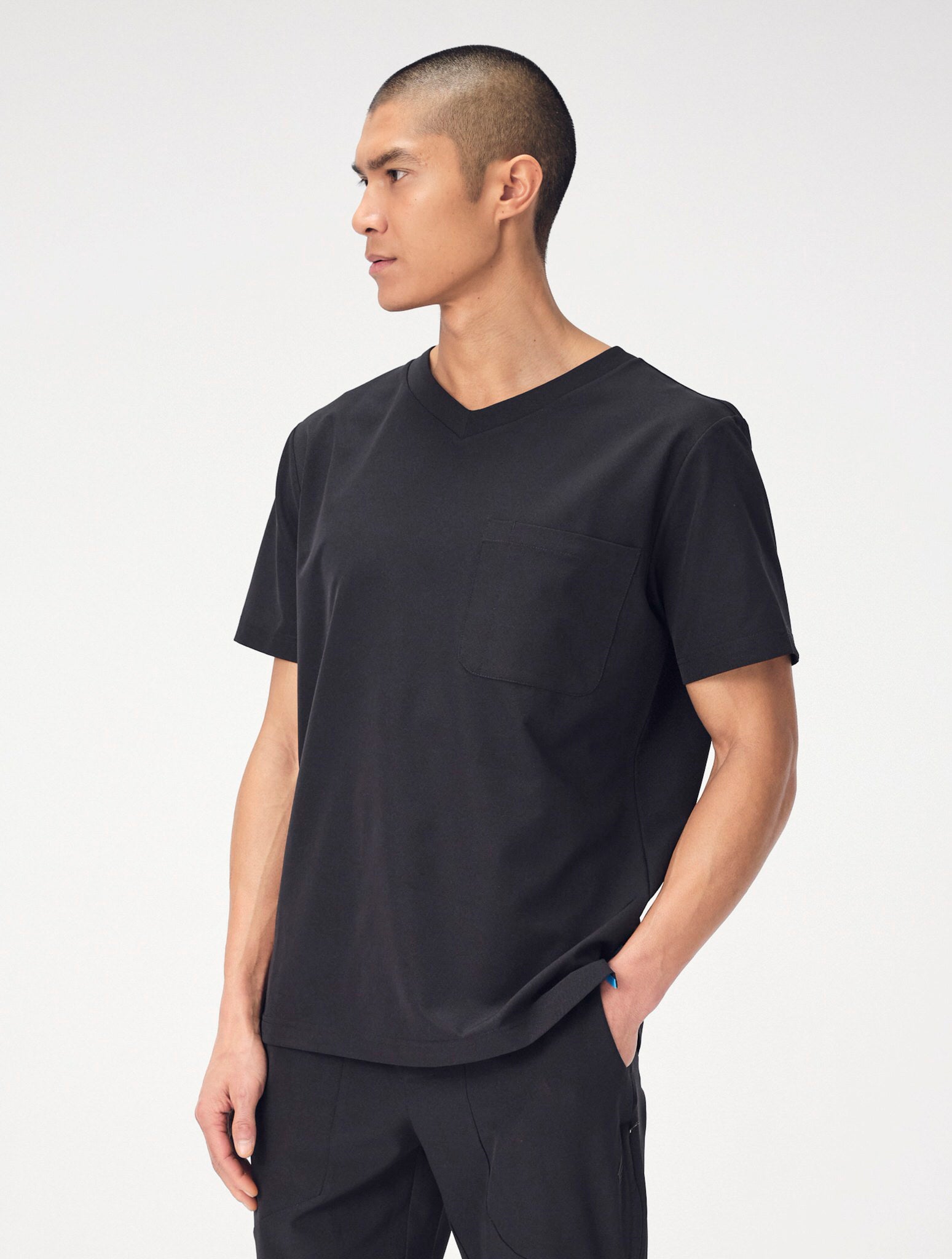 A man wearing a set of black Penna scrubs with his left hand posed in his pocket looks off to the right.