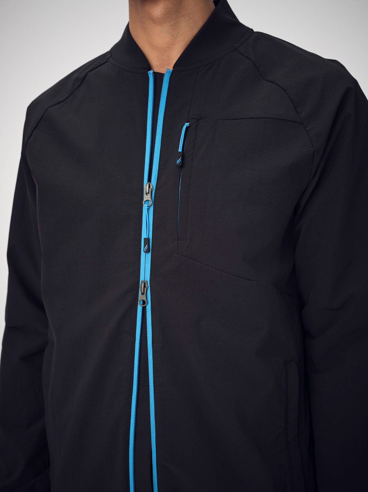 A close-up of a man's chest, wearing a black, stretch, bomber jacket with a bright blue two-way zipper up the front called The Eagle.