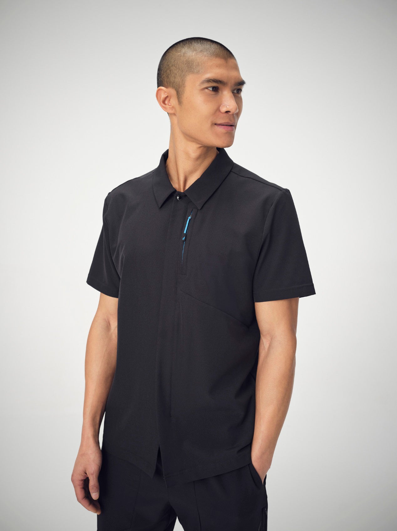 A man wearing black Penna scrubs from the knees up, posing with his left hand in his pocket looks off to the left.