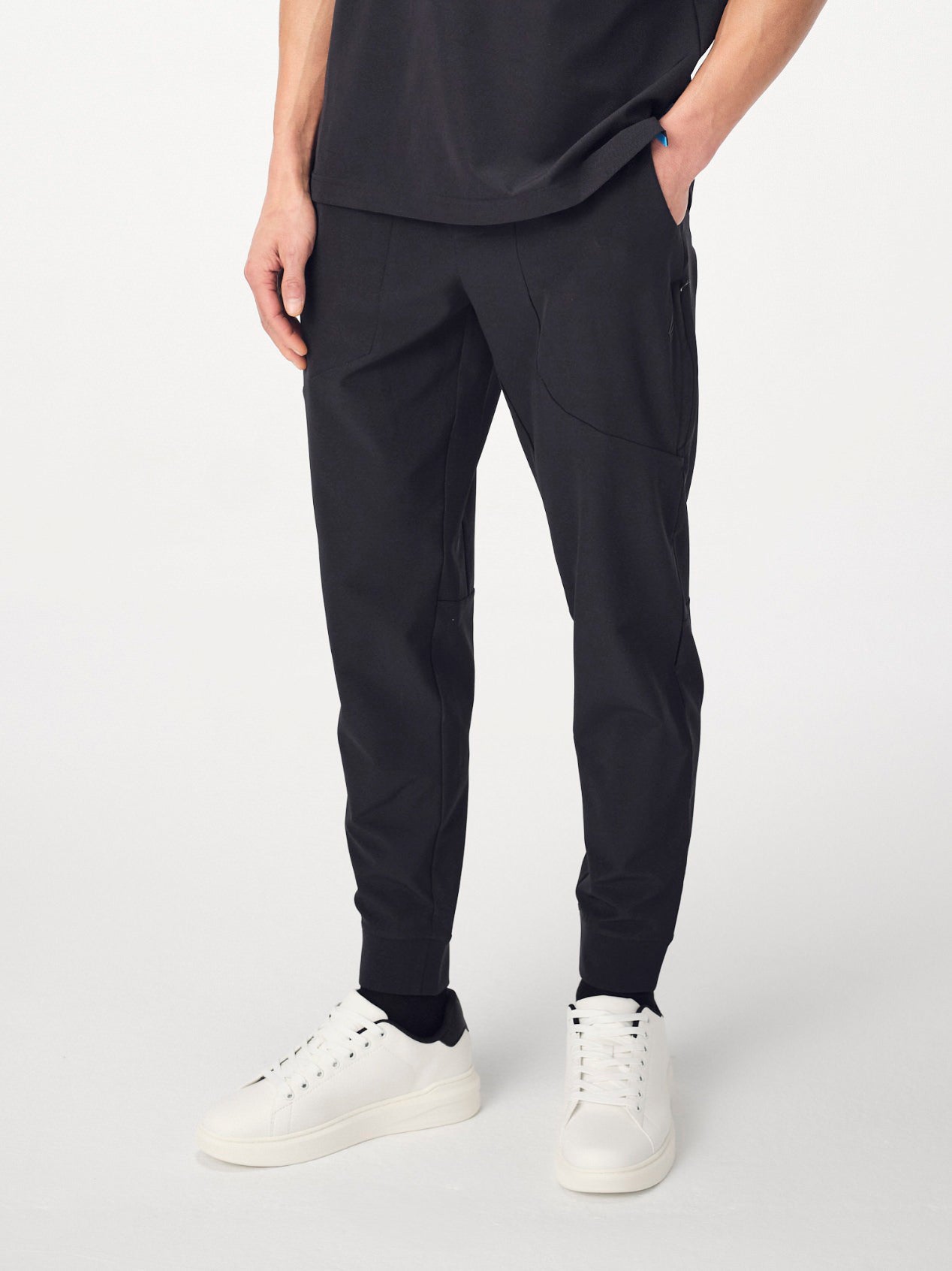 A man photographed from the waist-down wearing the Falcon jogger bottoms and white running shoes. He is posing with his right hand in his pocket and his left hand by his side.