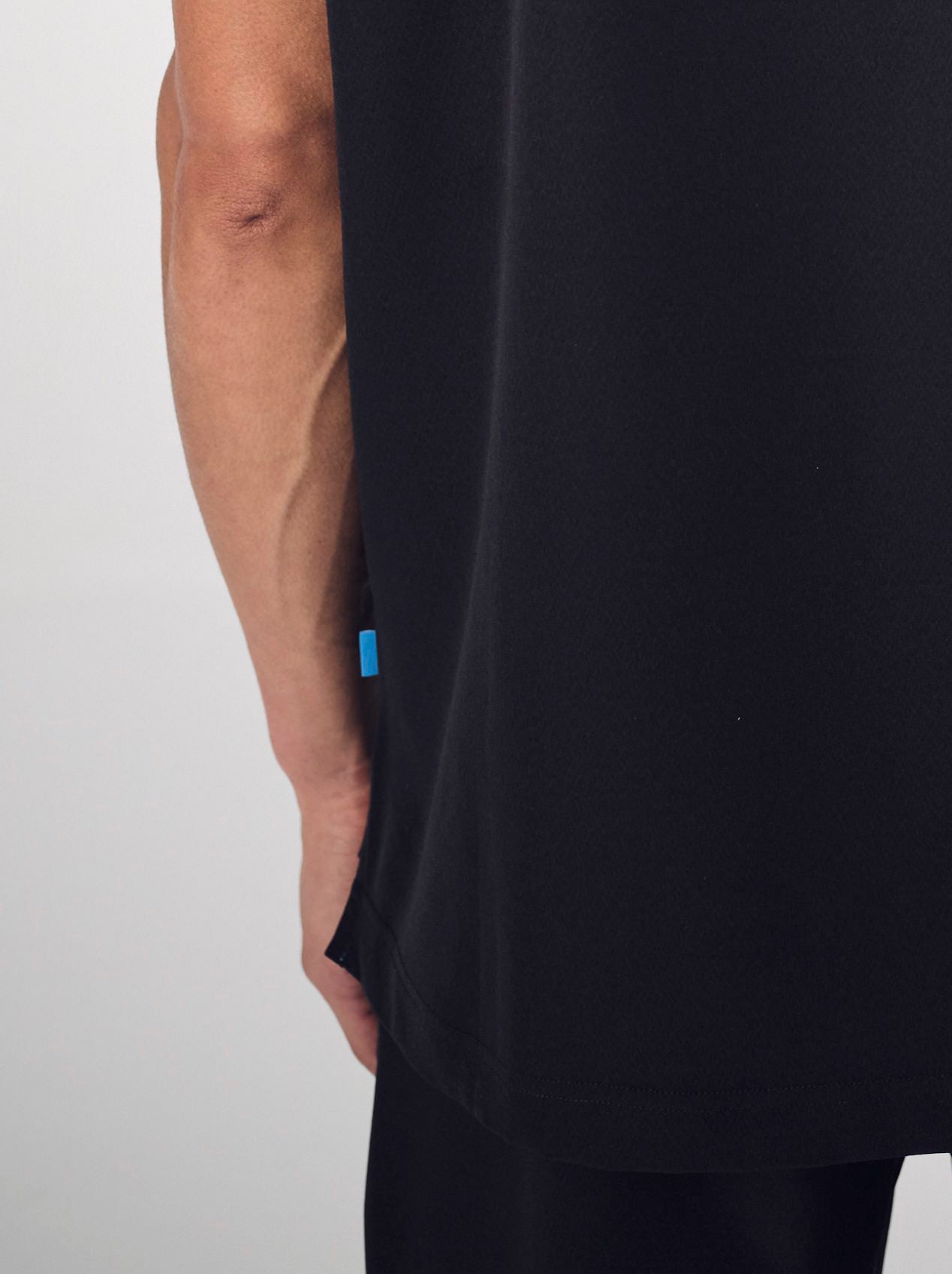 A close-up of a man's back wearing the black Penna scrub top style The Hawk, showing the shirt length hitting below the hips.