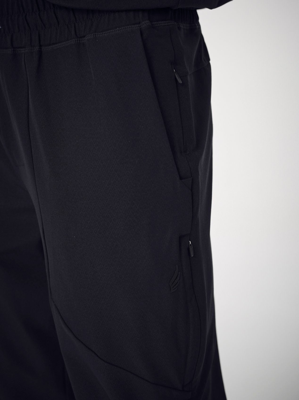 A close-up of a man's back wearing the black Penna scrub top style The Hawk tucked into the black jogger pants.