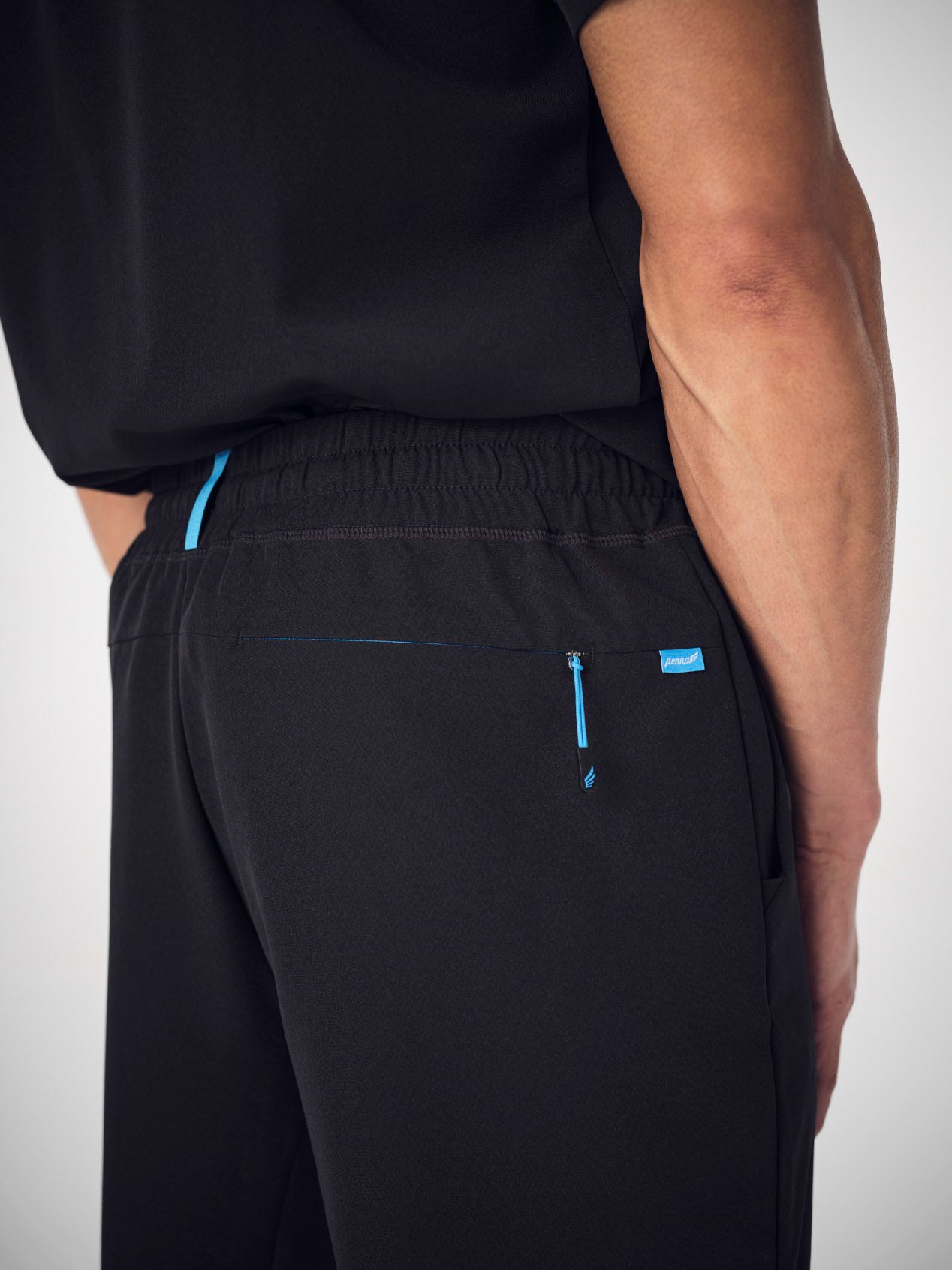 A closeup of a man's backside, wearing black Penna scrubs. He is wearing the Hawk style top tucked into the Falcon jogger bottoms.
