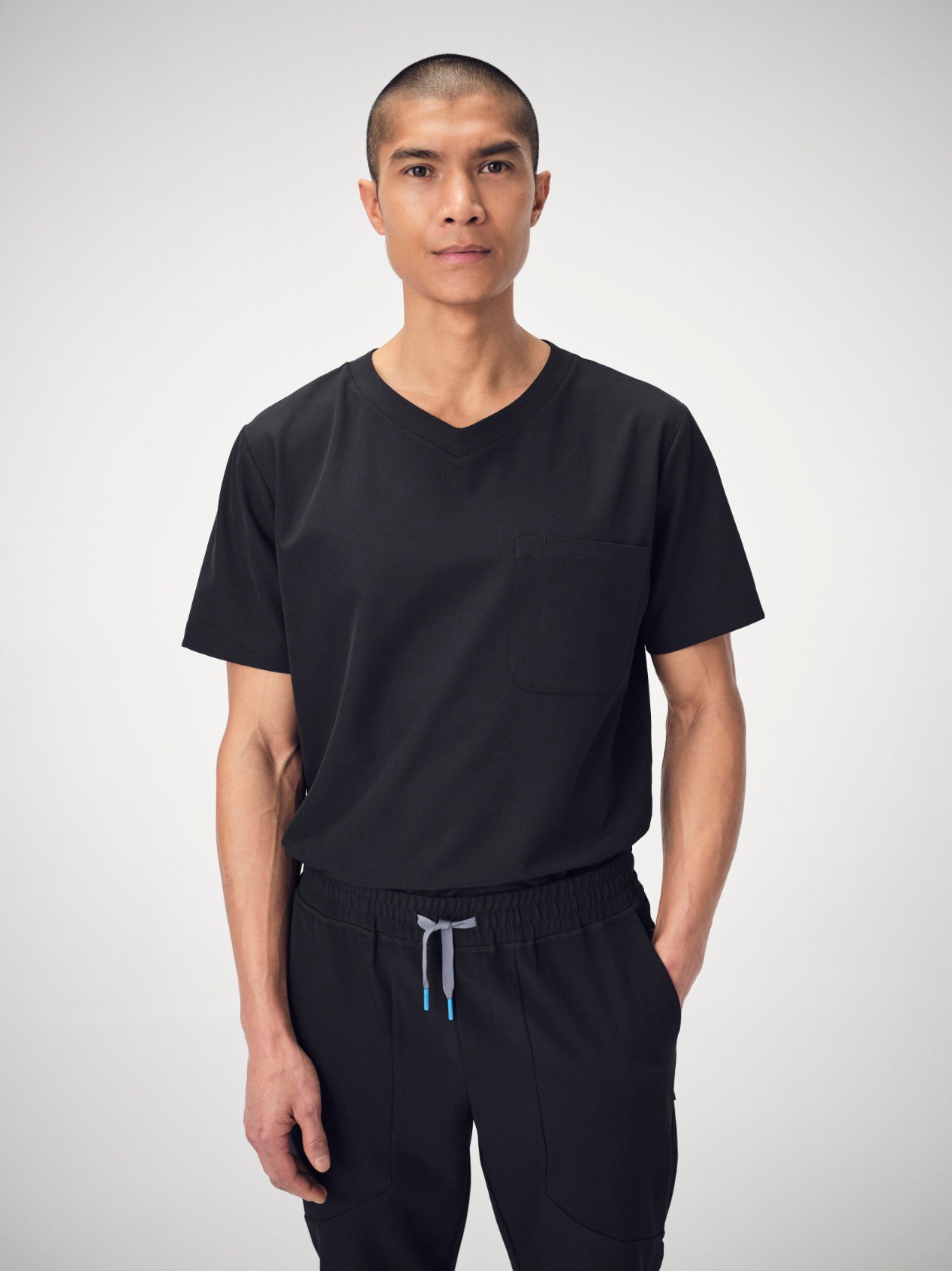 A man wearing black Penna scrubs from the knees up, posing with his left hand in his pocket.