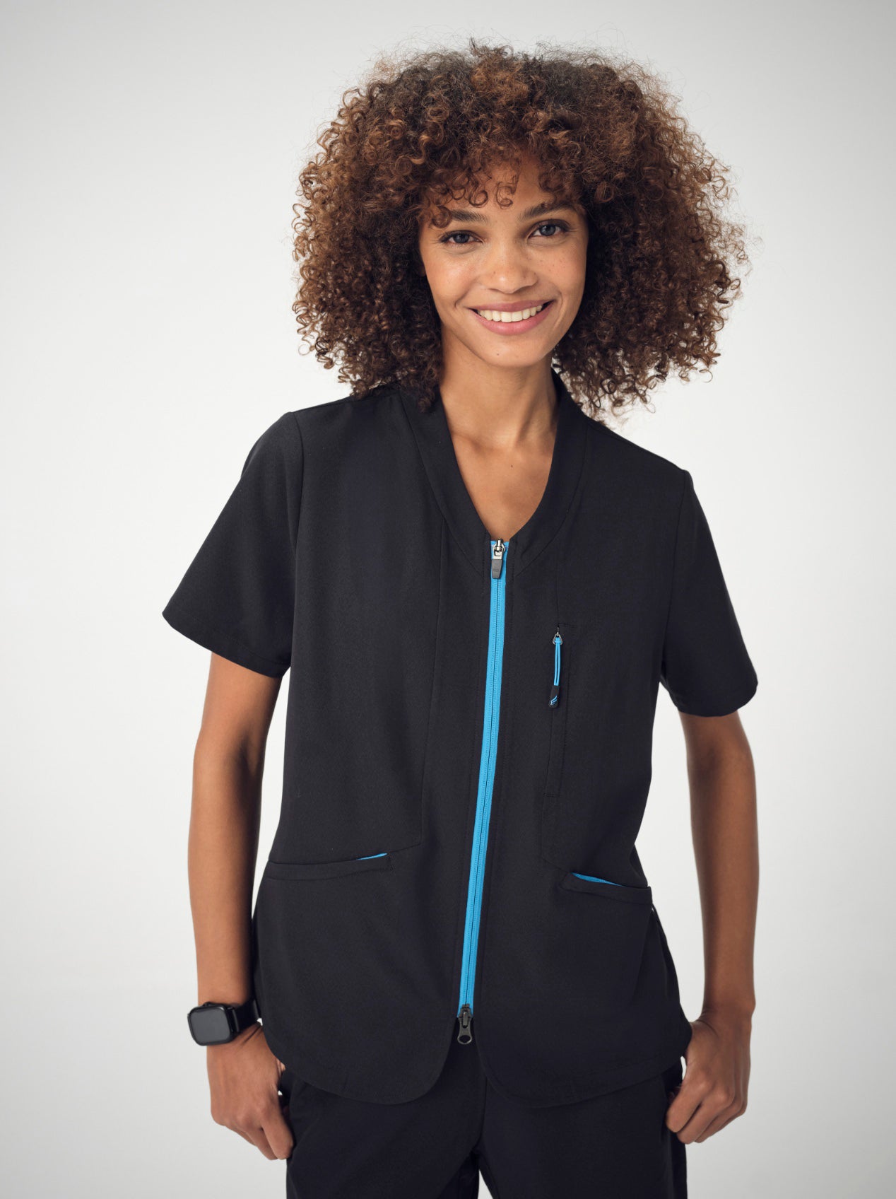 A woman photographed from the waist up, posing with her hands in her pockets, wearing the black Penna Skylark short-sleeved, pocket top.