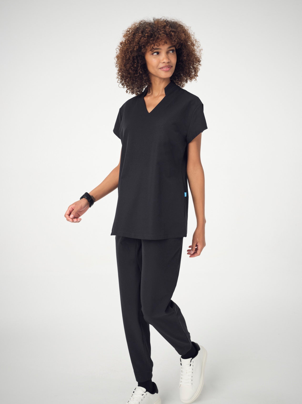 A woman photographed from the front wearing the black Penna Skylark short-sleeved, v-neck top, black jogger bottoms in the Dove style and white sneakers.