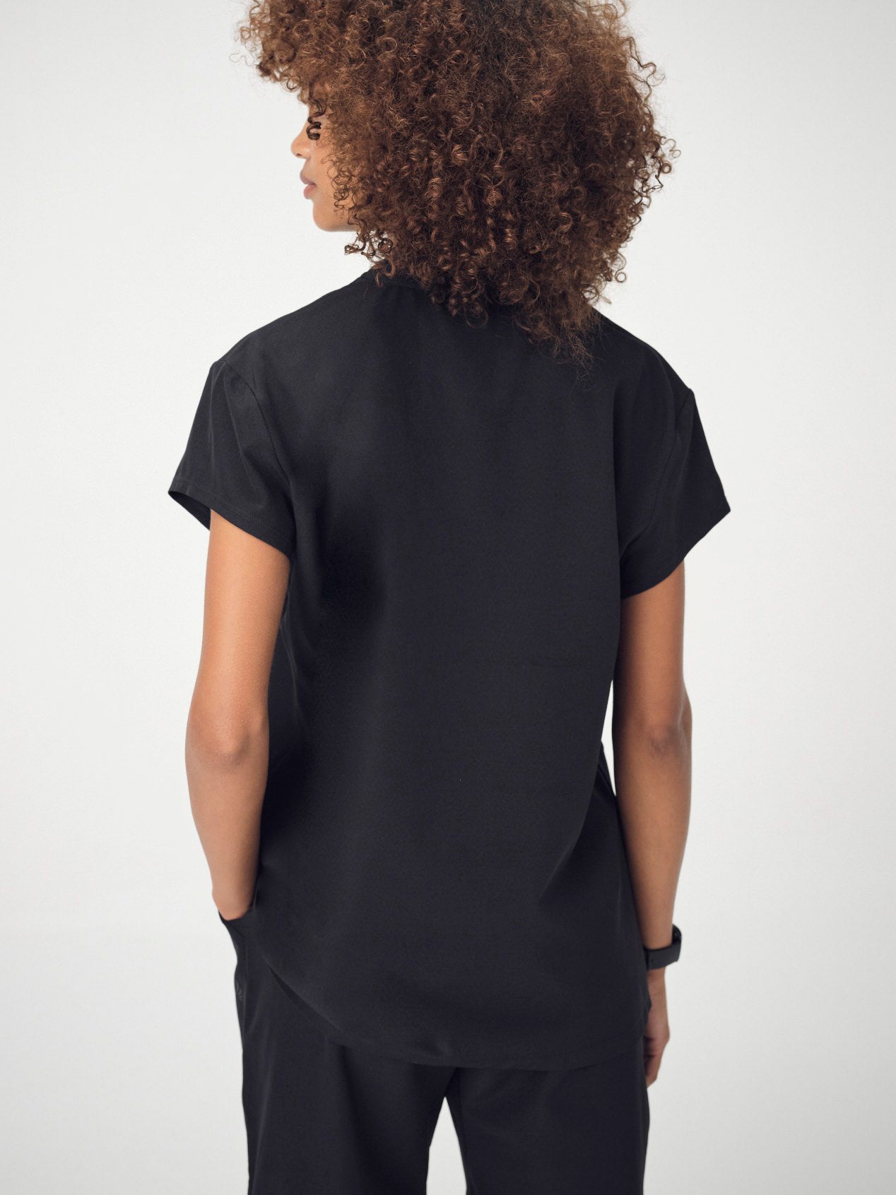 A woman photographed from behind wearing the black Penna Skylark short-sleeved, v-neck top and black jogger bottoms.