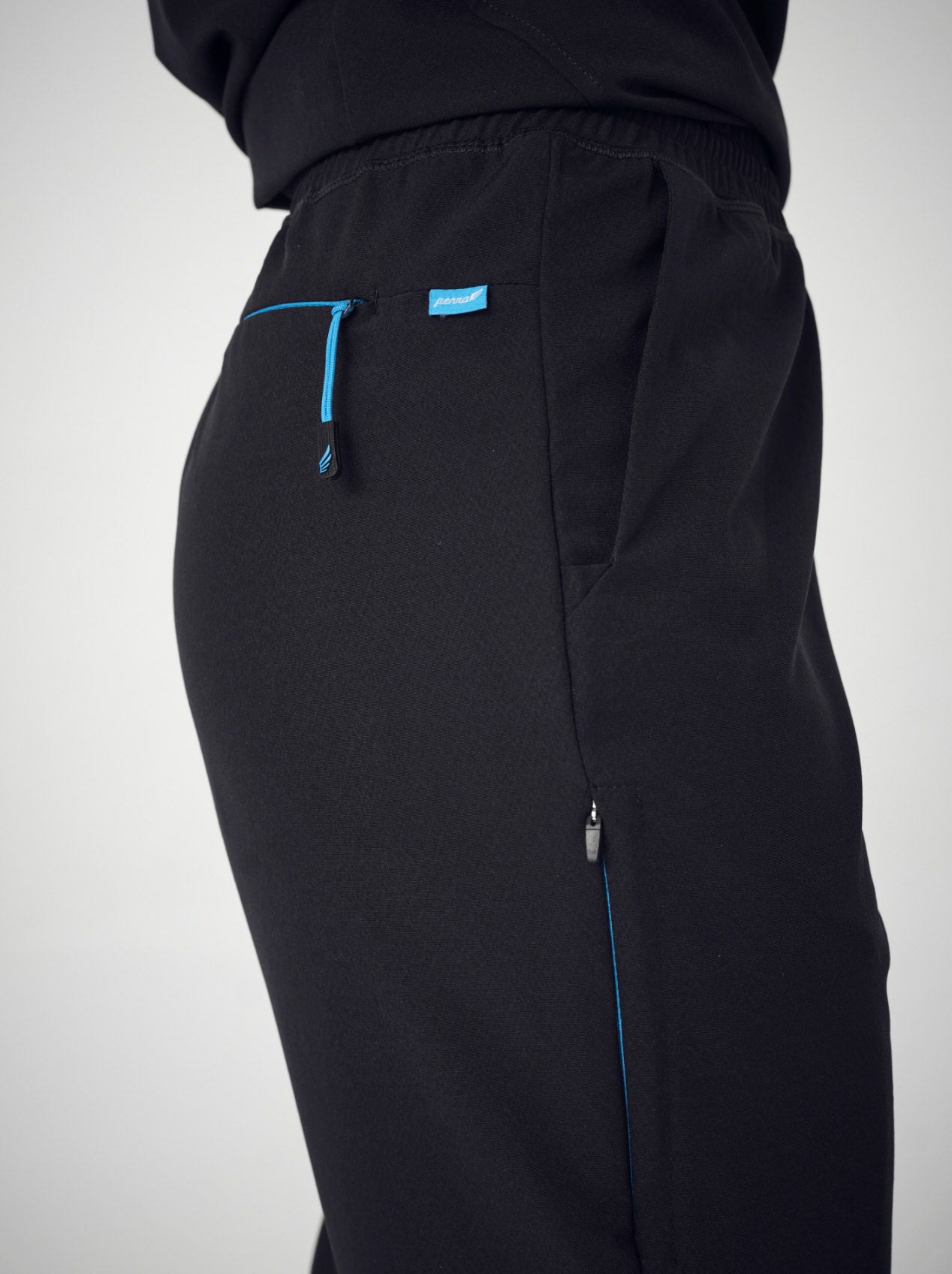 A closeup of from behind of a woman wearing a set of black Penna scrubs with the shirt tucked into the pants.