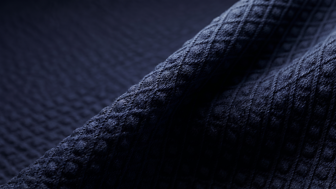 Close-up image of navy blue fabric with a textured, diamond jacquard pattern.