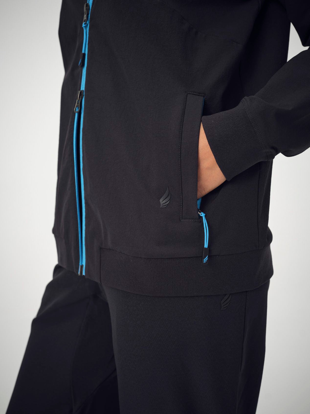 A close-up of a woman's torso wearing the black Penna bomber jacket The Hummingbird and The Dove jogger bottoms. The woman's hands are in her jacket pockets.