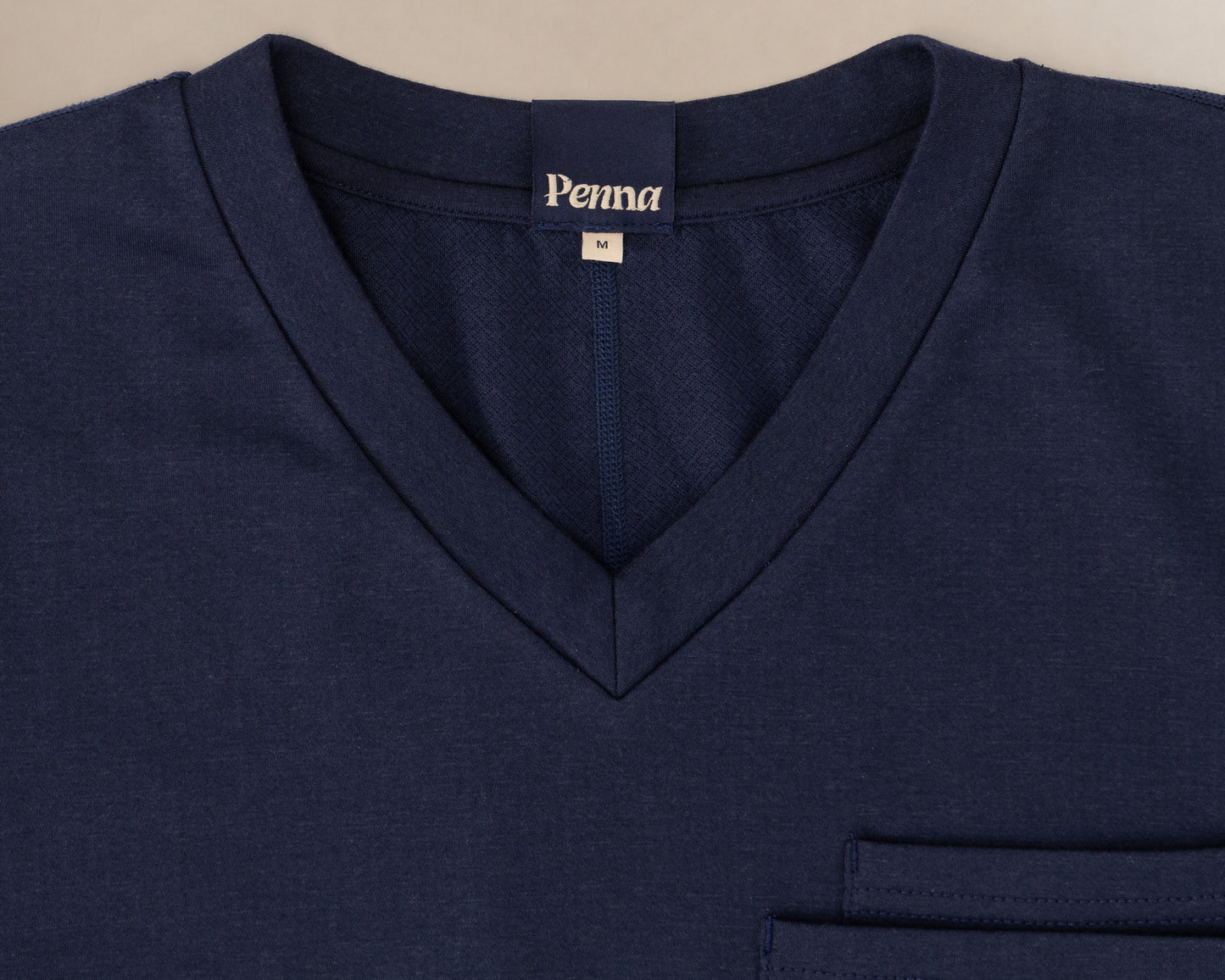 Close-up of a navy blue V-neck scrub t-shirt with a chest pocket and a visible 'Penna' brand label inside the collar.