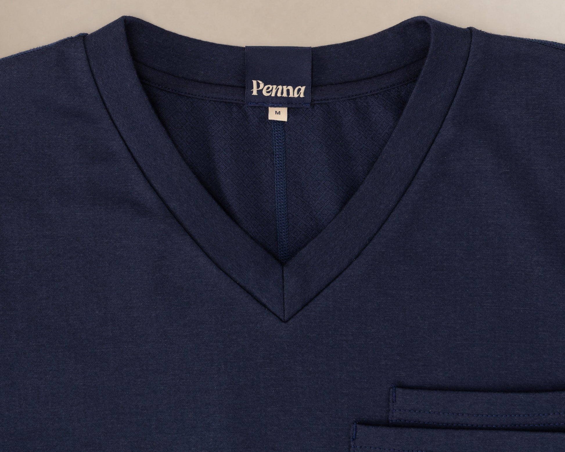 Close-up of a navy blue V-neck scrub t-shirt with a chest pocket and a visible 'Penna' brand label inside the collar.