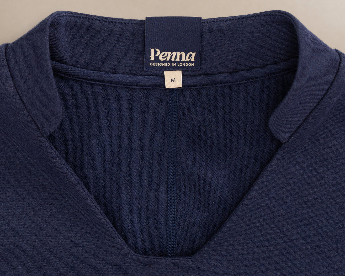 Close-up of the collar of a navy blue V-neck knit scrub top, showing the 'Penna' brand label and a size tag marked 'M'.