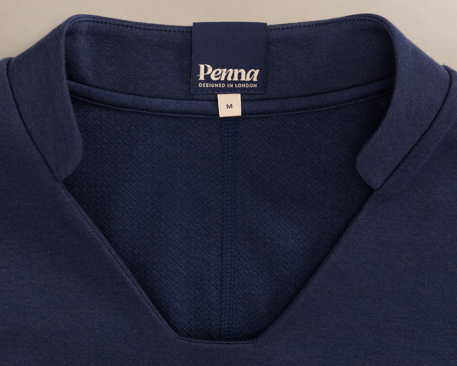 Close-up of the collar of a navy blue V-neck knit scrub top, showing the 'Penna' brand label and a size tag marked 'M'.