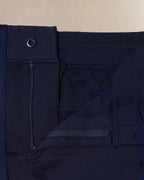 Close-up detail shot of dark navy blue scrub pants showing the waistband, button closure, belt loop, and front pocket stitching against a light beige background.