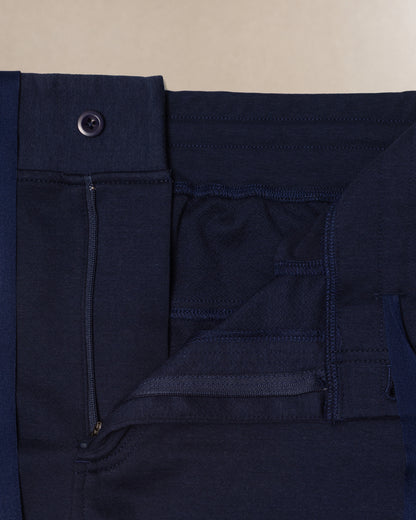 Close-up detail shot of dark navy blue scrub pants showing the waistband, button closure, belt loop, and front pocket stitching against a light beige background.