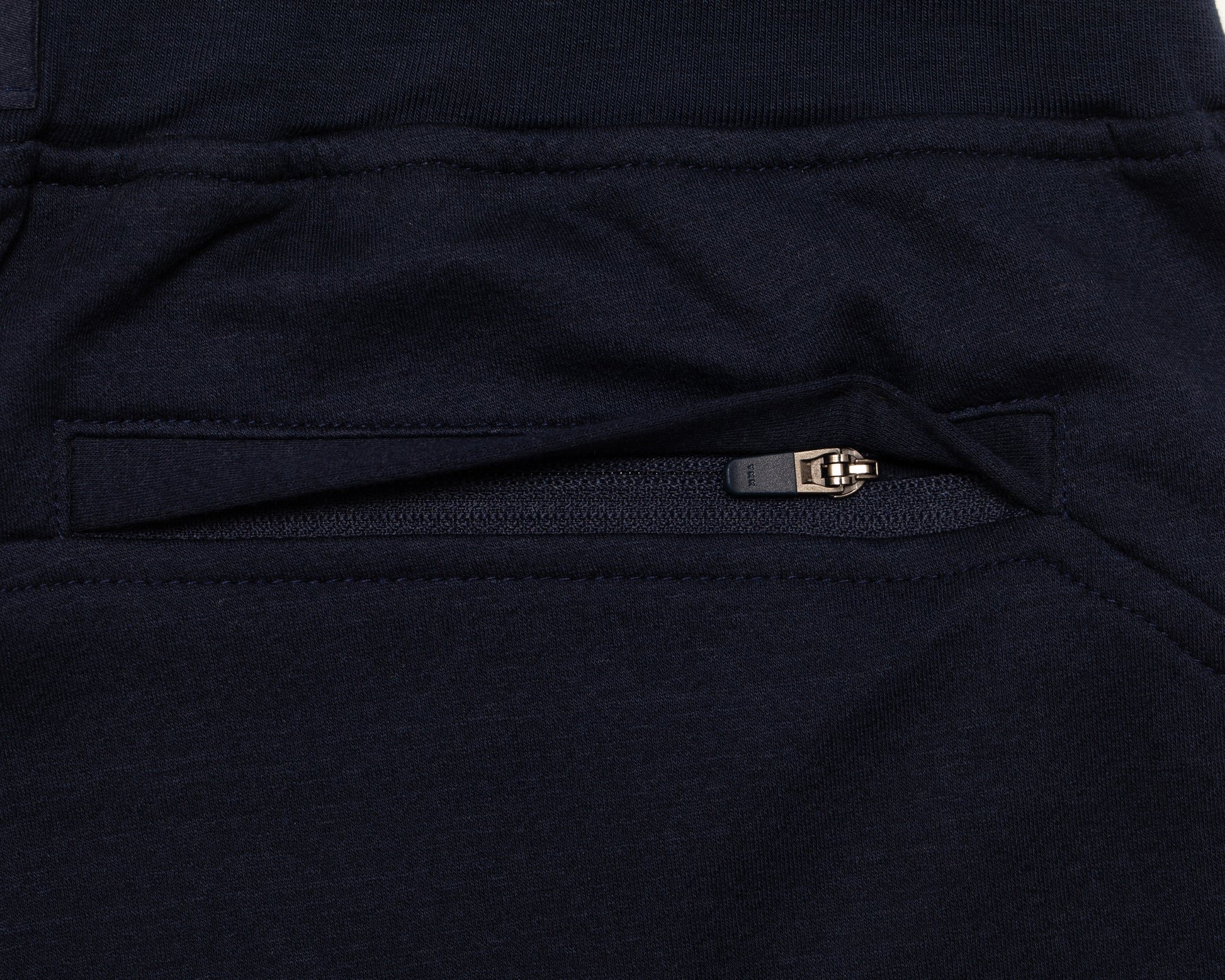 Close-up of a dark navy fabric garment showing a zippered pocket with a small metallic zipper pull.
