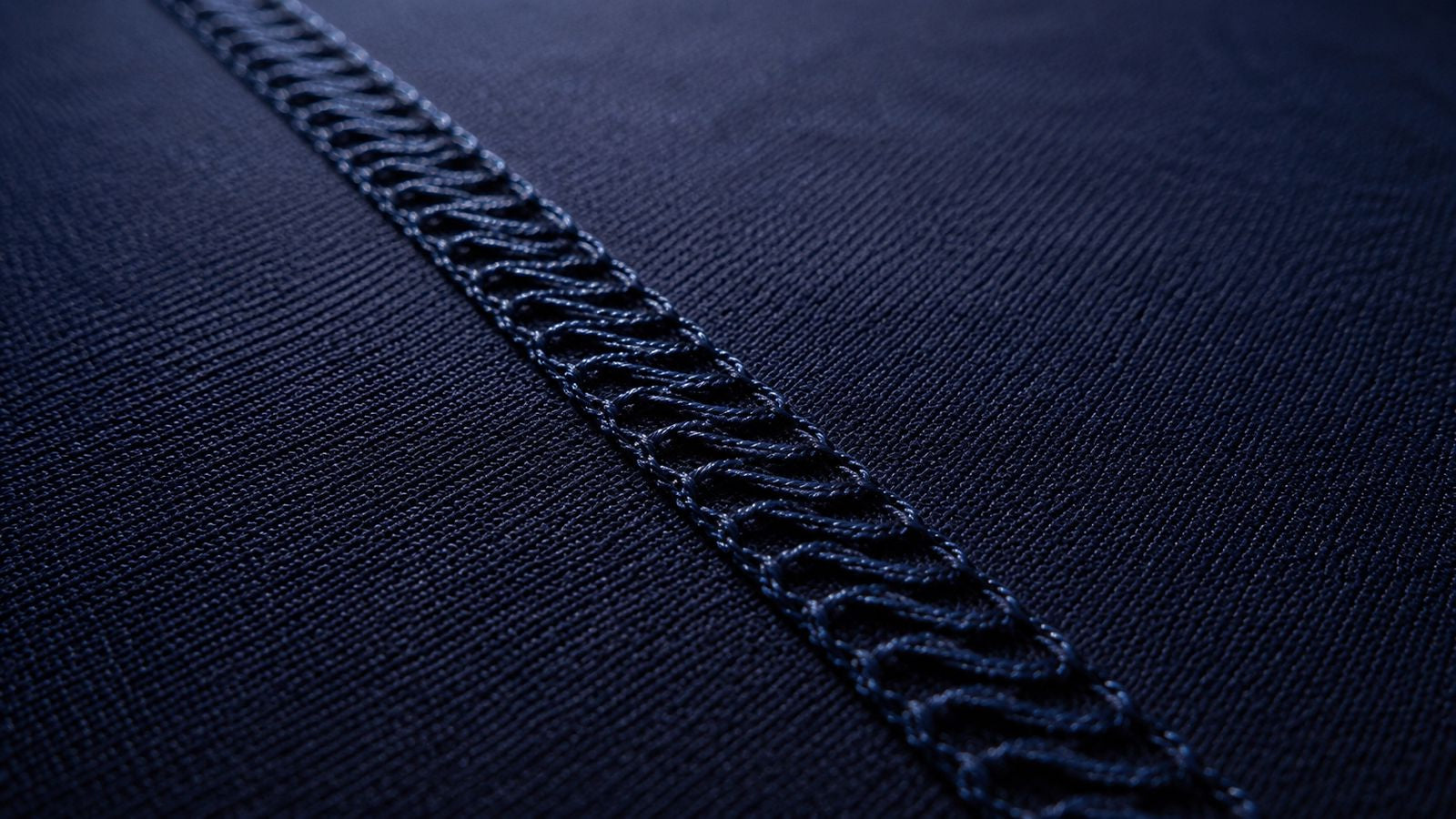 Close-up of dark navy blue textured fabric with a prominent decorative zigzag stitched seam running diagonally across the frame.