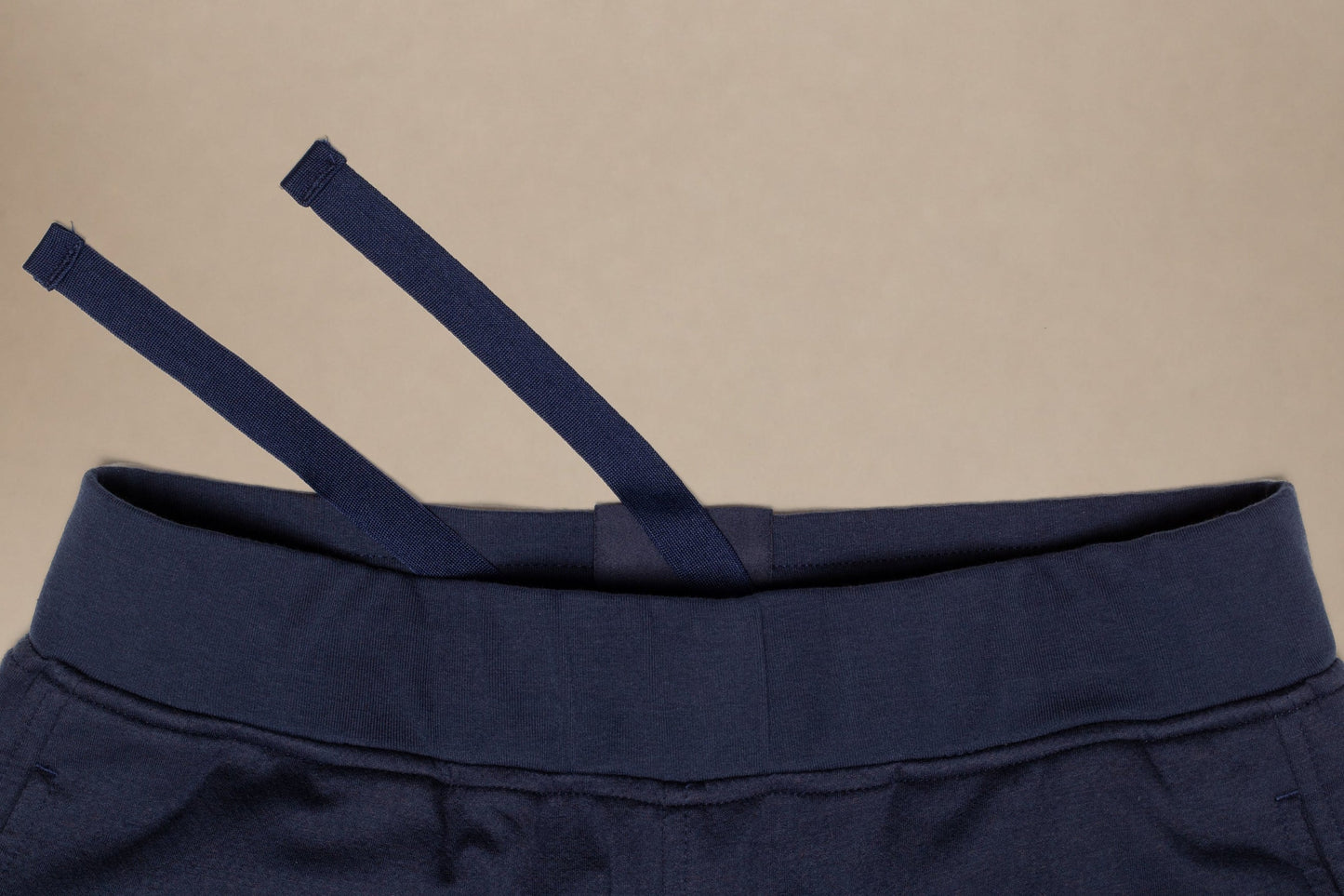 Close-up of a navy blue garment, likely sweatpants or shorts, showing the elastic waistband and drawstring against a plain beige background.