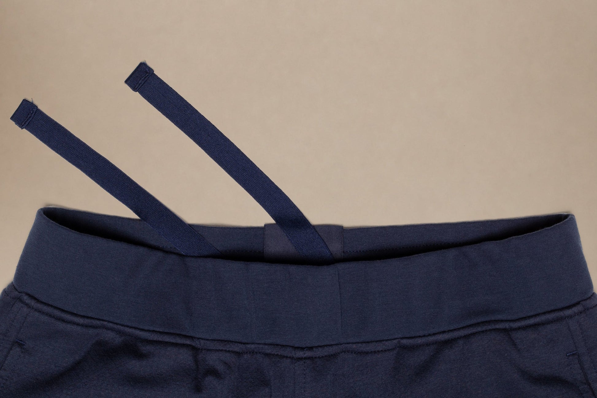 Close-up of a navy blue garment, likely sweatpants or shorts, showing the elastic waistband and drawstring against a plain beige background.
