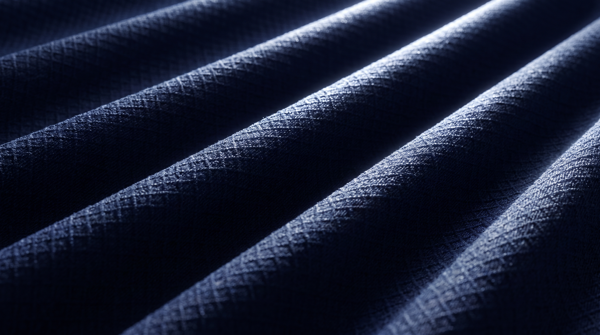A close-up of dark navy blue textured fabric with diagonal pleated folds and a subtle woven pattern.