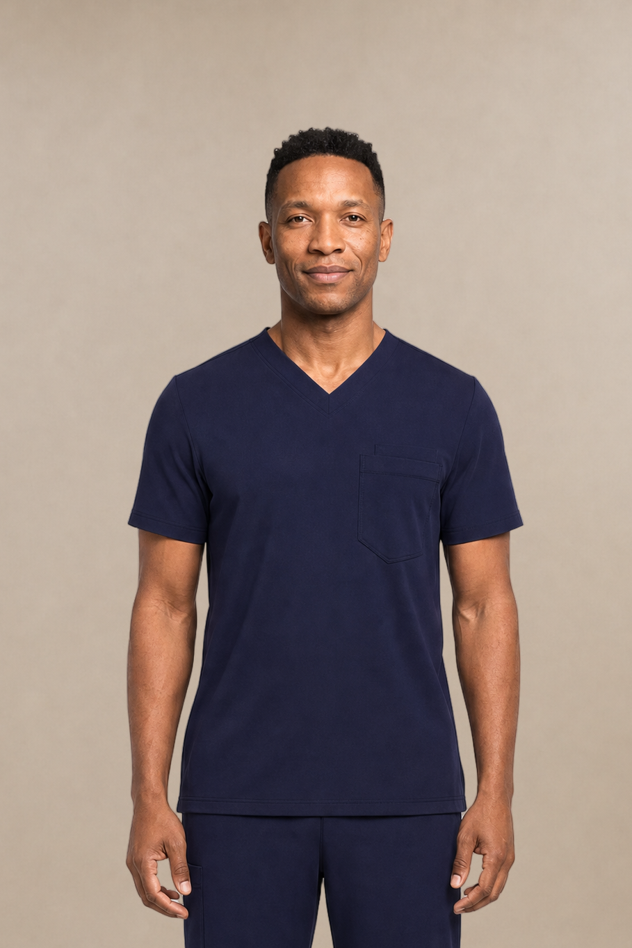 A man modeling a navy blue V-neck scrub top and matching scrub pants set, standing against a neutral beige studio background.