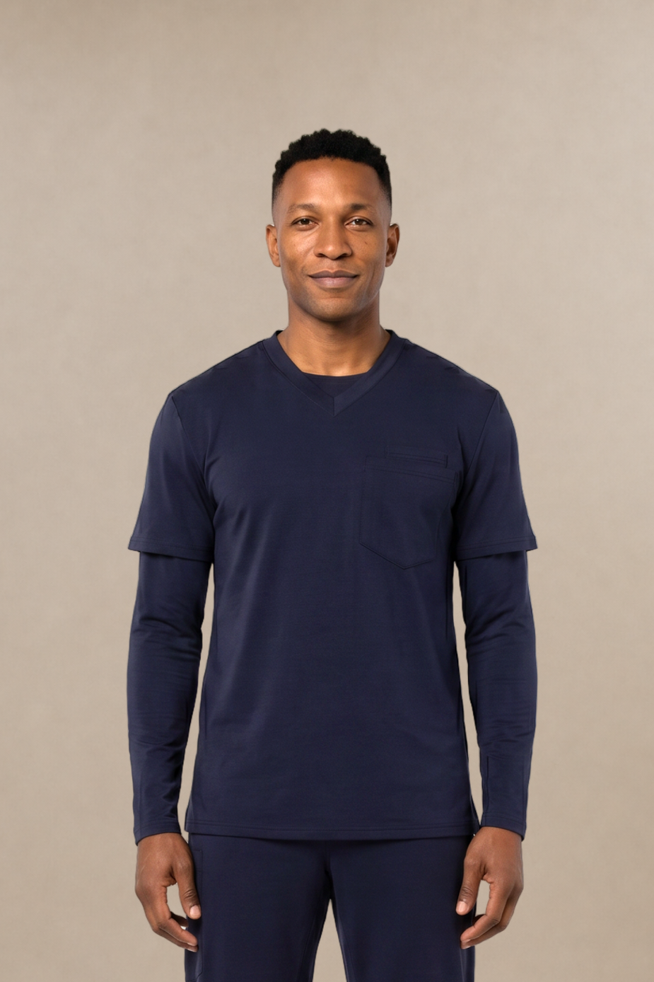 A man modeling a matching navy blue long-sleeve shirt and scrub pants set, standing against a solid beige studio background.