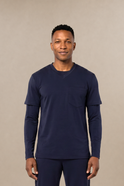 A man modeling a matching navy blue long-sleeve shirt and scrub pants set, standing against a solid beige studio background.