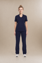 A woman modeling a matching navy blue scrub set consisting of a short-sleeve V-neck top and straight-leg pants, standing against a solid beige studio background.