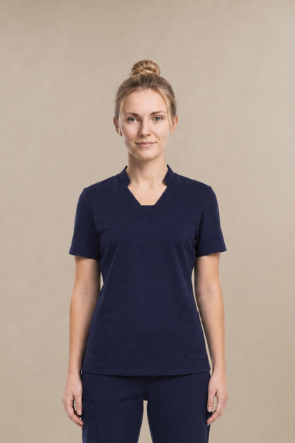 A woman modeling a matching navy blue scrub set consisting of a short-sleeve V-neck top and straight-leg pants, standing against a solid beige studio background.