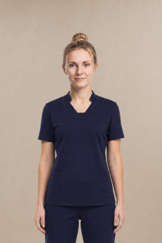 A woman modeling a matching navy blue scrub set consisting of a short-sleeve V-neck top and straight-leg pants, standing against a solid beige studio background.