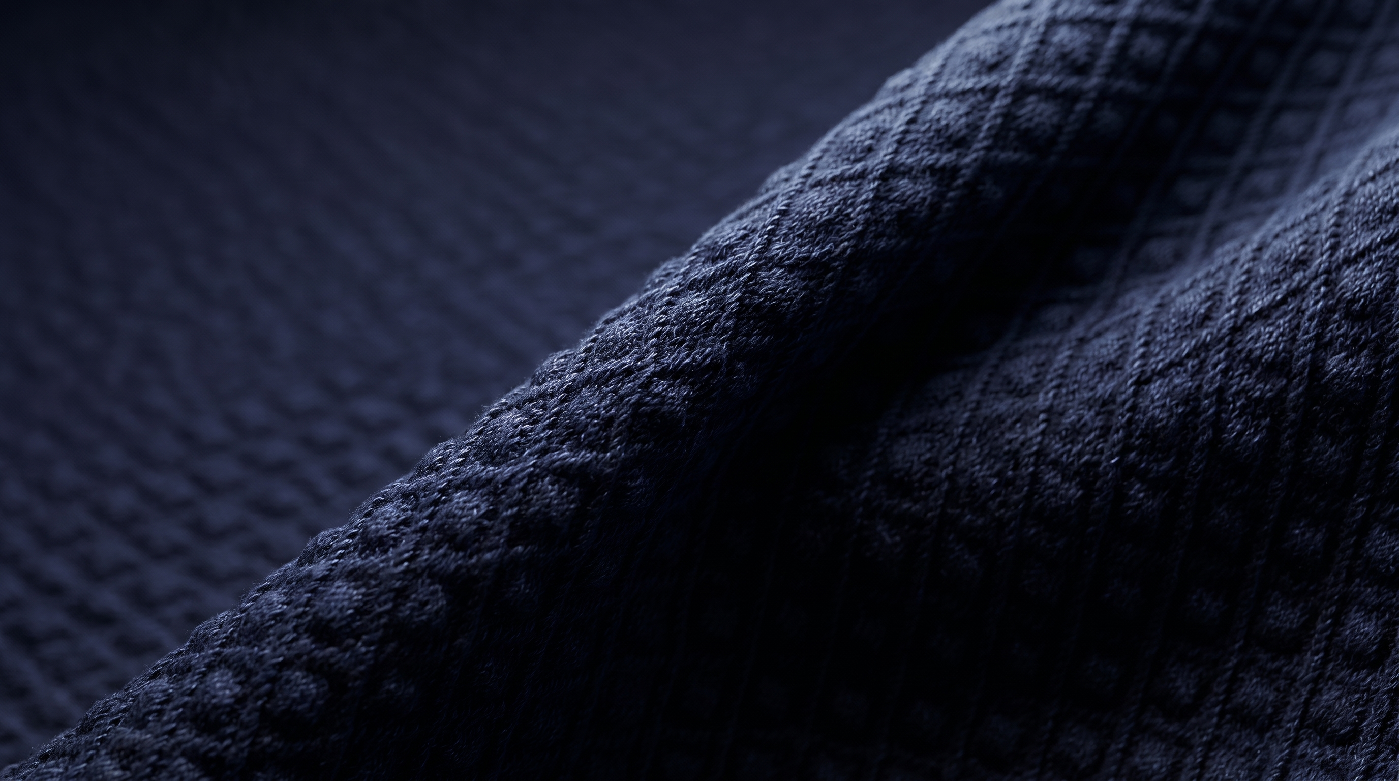Close-up of a dark navy blue textured fabric, showing a waffle or diamond knit pattern with soft folds and shadows.