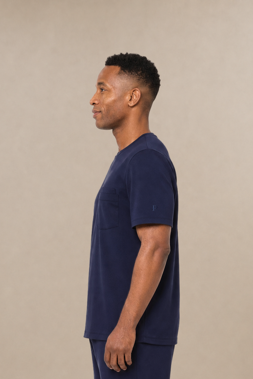 A man in profile wearing a navy blue short-sleeve t-shirt and matching navy blue sweatpants, standing against a plain beige studio background.