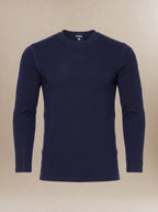 A men's, navy blue long-sleeve crewneck underscrub top displayed on a neutral beige background.
